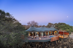 Un moderno lodge de varios niveles con una amplia terraza y piscina, rodeado de vegetación exuberante.