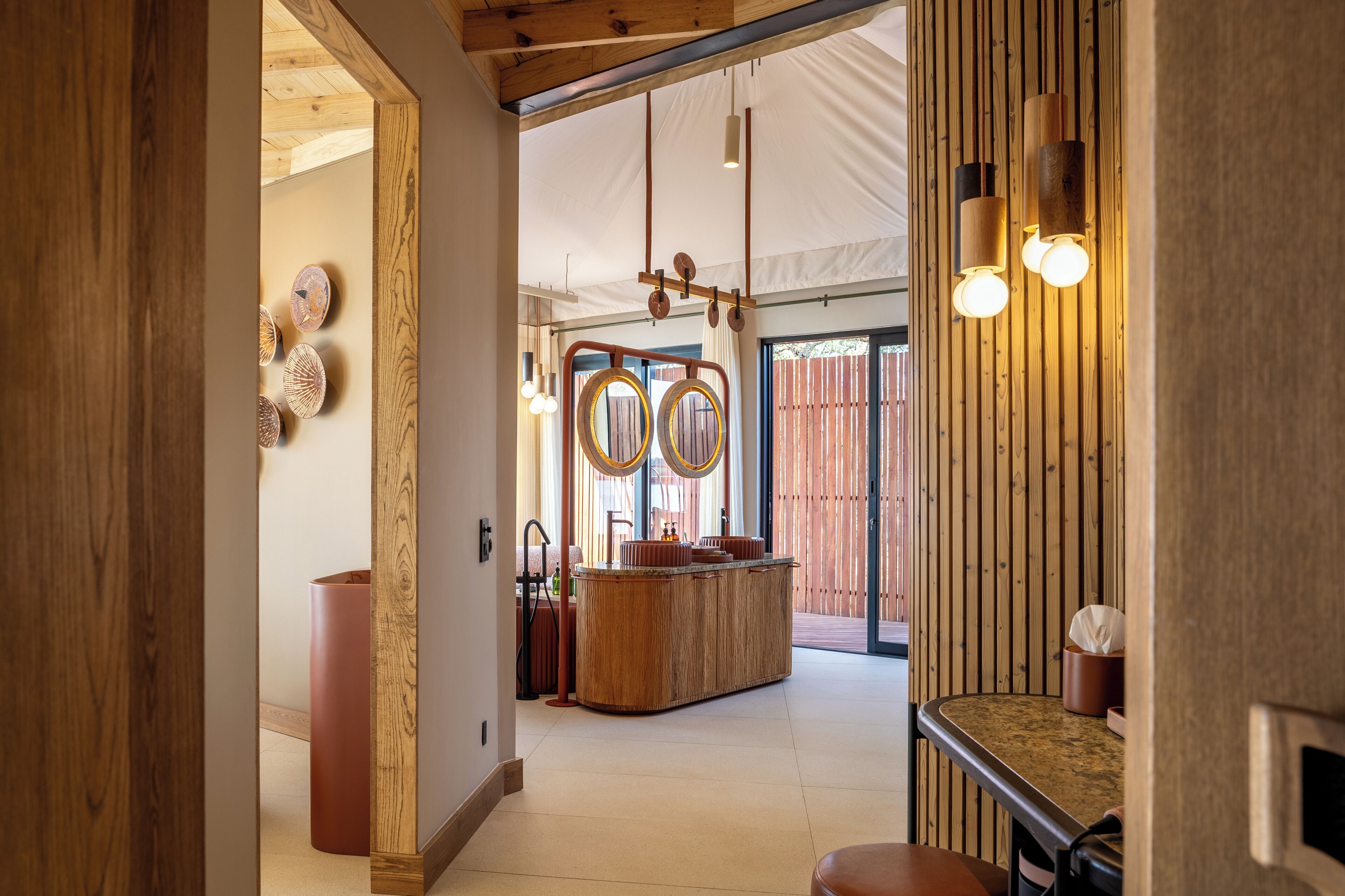 A corridor with a wooden floor, a round wooden table with a mirror, and a hanging light fixture.