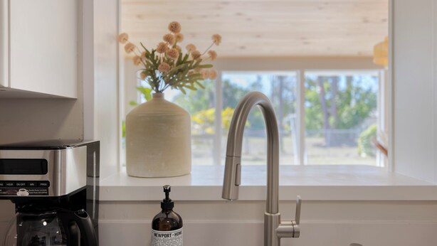 A kitchen with a coffee maker, a vase with flowers, and a window with a view of greenery. - Casa del Sol - Venice Island Beach Escape (Venice)