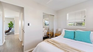 A bedroom with a bed, a bedside table, a window with blinds, a door leading to another room, and a plant in the corner. - Casa del Sol - Venice Island Beach Escape (Venice)