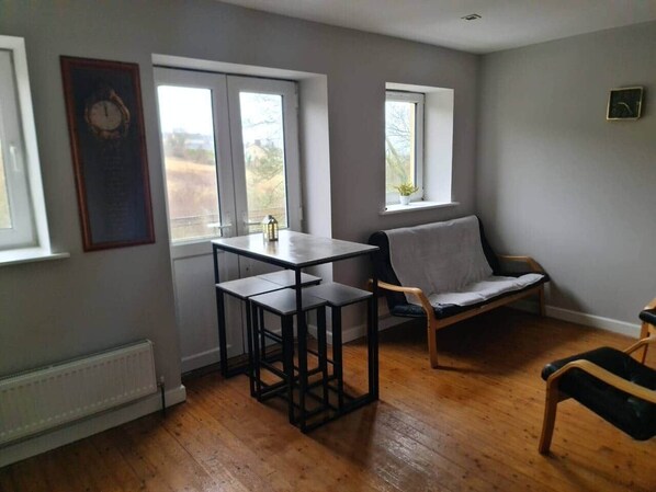 A room with a table and chairs, a radiator, and two windows.