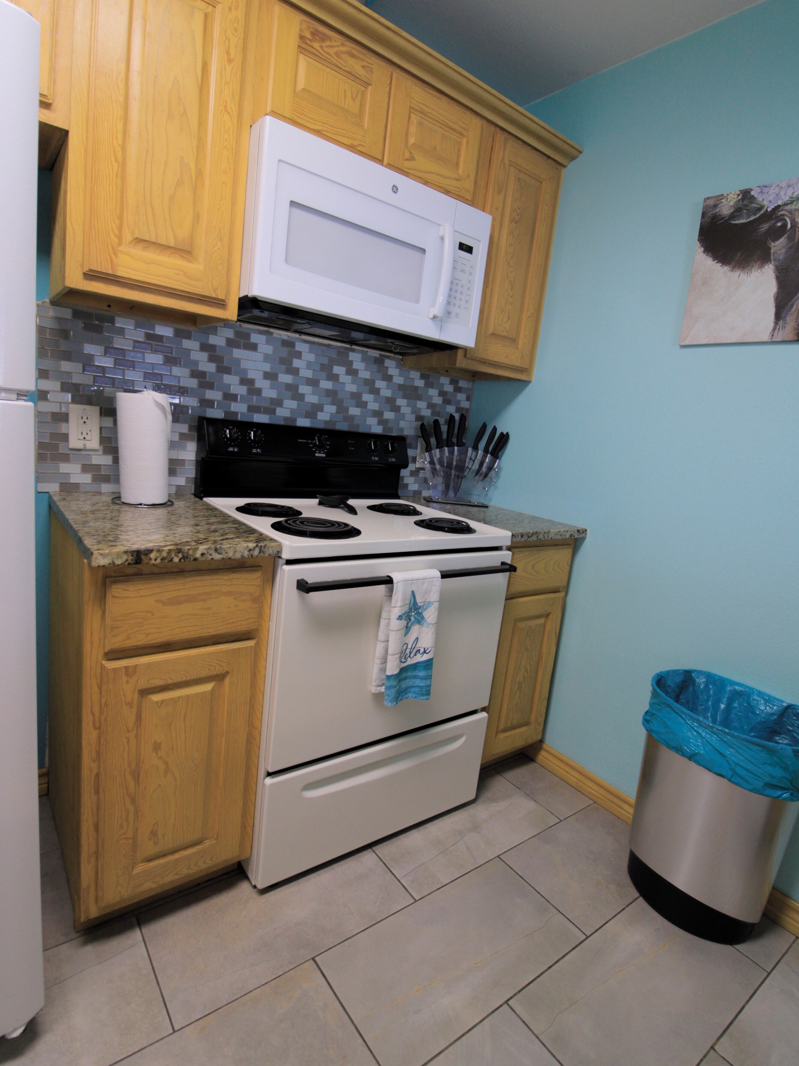A kitchen with wooden cabinets, a white stove, a microwave, and a trash can.