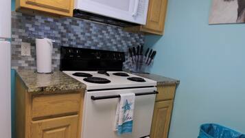 A kitchen with wooden cabinets, a white stove, a microwave, and a trash can.