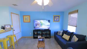 A living room with a sofa, a coffee table, a TV, and a small table with a laptop.