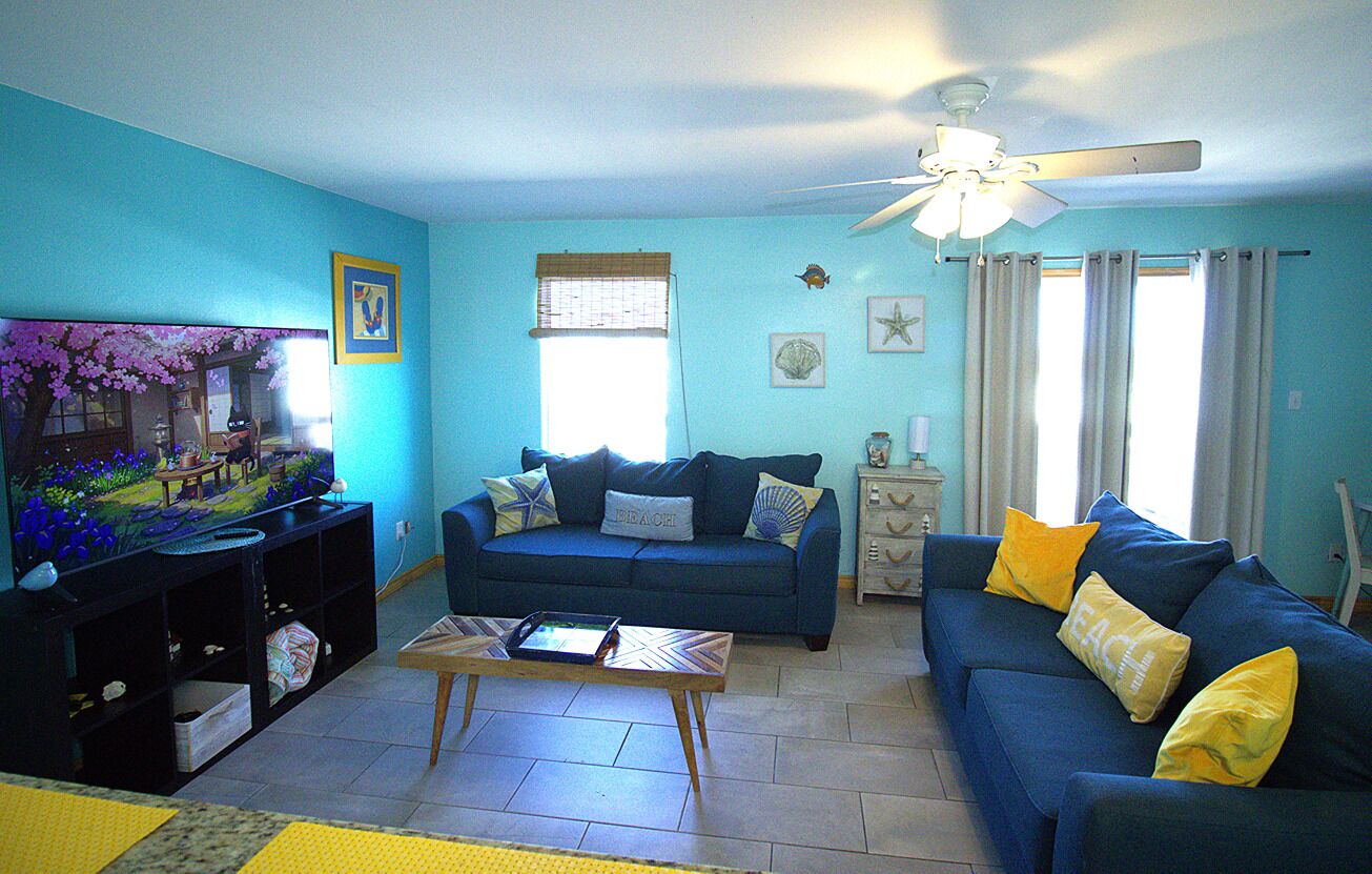 A living room with a blue sofa, a coffee table, a television, and a ceiling fan.
