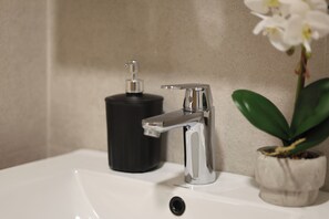 Ein Badezimmerwaschbecken mit chromfarbenem Wasserhahn, einem schwarzen Seifenspender und einer Orchidee im Topf.