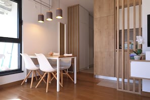 Ein moderner Essbereich mit Holztisch, weißen Stühlen, Pendelleuchten und Blick durch ein Fenster.