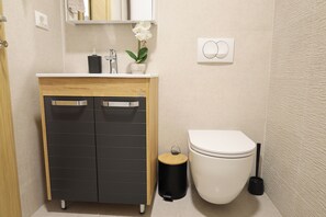 Une salle de bain moderne avec un meuble-lavabo en bois, des toilettes blanches et une petite poubelle.