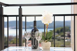 Ein Balkon mit Tisch, einer Weinflasche, zwei Gläsern und einem Topf mit einer Orchidee.