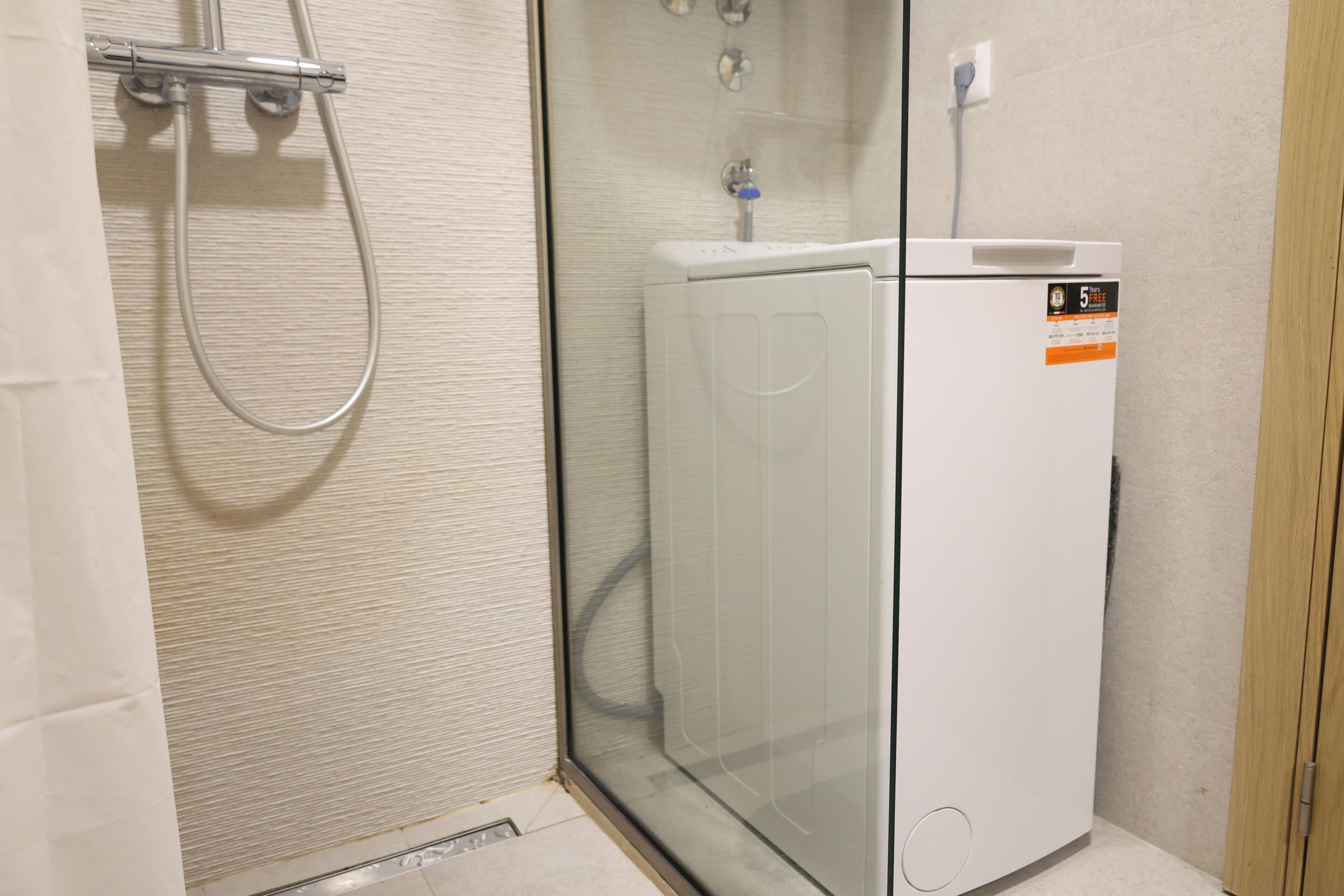 A compact, modern bathroom with a glass shower enclosure, a white washing machine, and a visible electrical outlet.