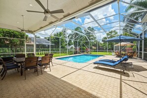 Ein überdachter Außenbereich mit Pool, Liegestühlen und einem Tisch mit Stühlen.