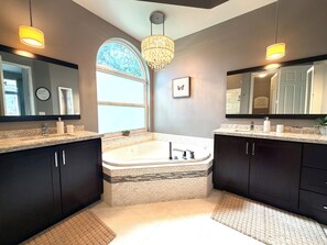 Ein modernes Badezimmer mit einer großen Badewanne, zwei Waschbecken, dunklen Schränken und einer Deckenleuchte.