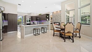 Una cocina moderna con armarios oscuros, una isla central y un comedor con sillas ornamentadas.