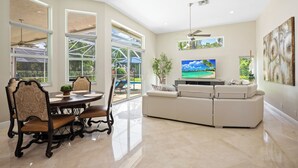 Un salón amplio con un televisor grande, un sofá y una zona de comedor con sillas.