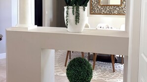 Una consola blanca con dos macetas blancas, una con orquídeas blancas y otra con follaje verde, y un pequeño topiario.