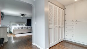 A bedroom with a bed, a ceiling fan, a wardrobe, and a desk with a lamp.