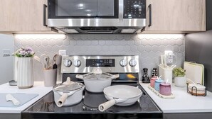 A modern kitchen with a stainless steel stove, microwave, and oven. There are pots and pans on the stove, a vase with flowers, and various kitchen utensils on the counter. - New Fremont Designer 3BR TH w/ Rooftop View & King (Seattle)