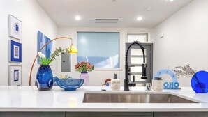 A modern kitchen with a stainless steel sink, a yellow pendant light, and a window with blinds. - New Fremont Designer 3BR TH w/ Rooftop View & King (Seattle)