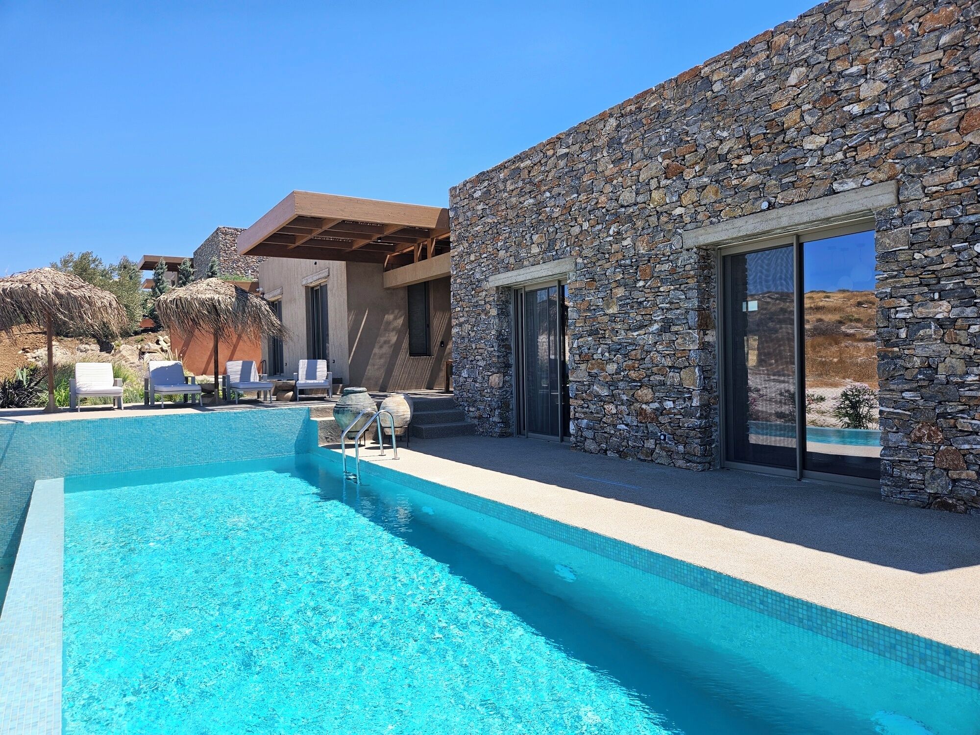 Ein moderner Poolbereich mit Steinwand, Liegestühlen und einem klaren, blauen Pool.