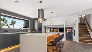 A modern kitchen with a large island, bar stools, and a view of palm trees. - Majestic Luxury Retreat | Pool ·Dome · Mini Golf (Joshua Tree)