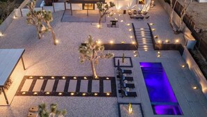 A pool area with a blue-lit water feature, seating, and desert plants. - Majestic Luxury Retreat | Pool ·Dome · Mini Golf (Joshua Tree)