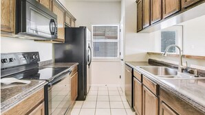 Una cocina con armarios de madera, un refrigerador negro, un microondas, una estufa y un lavabo.