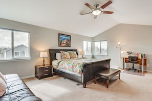 A bedroom with a bed, bedside tables, a desk, a chair, a ceiling fan, and large windows.