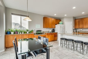 A modern kitchen with wooden cabinets, a glass dining table, and bar stools.