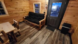 Ein Holzblockhaus-Innenraum mit einer Couch, einem kleinen Tisch, einer Tür und einem Fenster.