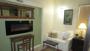 Una sala de estar con una pared verde, un sofá blanco, una silla de madera, una mesita, un cuadro enmarcado y una lámpara.