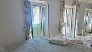 Ein Schlafzimmer mit Bett, Vorhängen, einer Pendelleuchte und Blick durch eine Glastür.