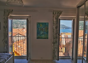 A room with a large window, a painting on the wall, and a bed. - Au Nid d'Azur, historic center of Menton - ocean view (Menton)