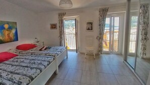 Ein Schlafzimmer mit einem Bett, einem Sessel, einem Gemälde und Blick durch eine Tür.