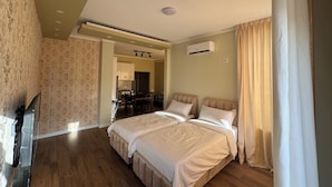 A hotel room with a double bed, a TV, a kitchenette, and a bathroom.