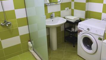 A small, clean bathroom with a shower, sink, and washing machine.