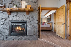 Una chimenea de piedra con fuego, una cama de madera y una puerta de madera.