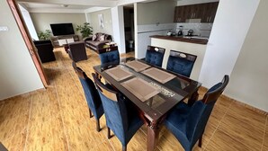 A dining area with a rectangular table, blue upholstered chairs, and a kitchen in the background. - Santa Ana Home, ideal para tu viaje en grupo o familia. (Cusco)