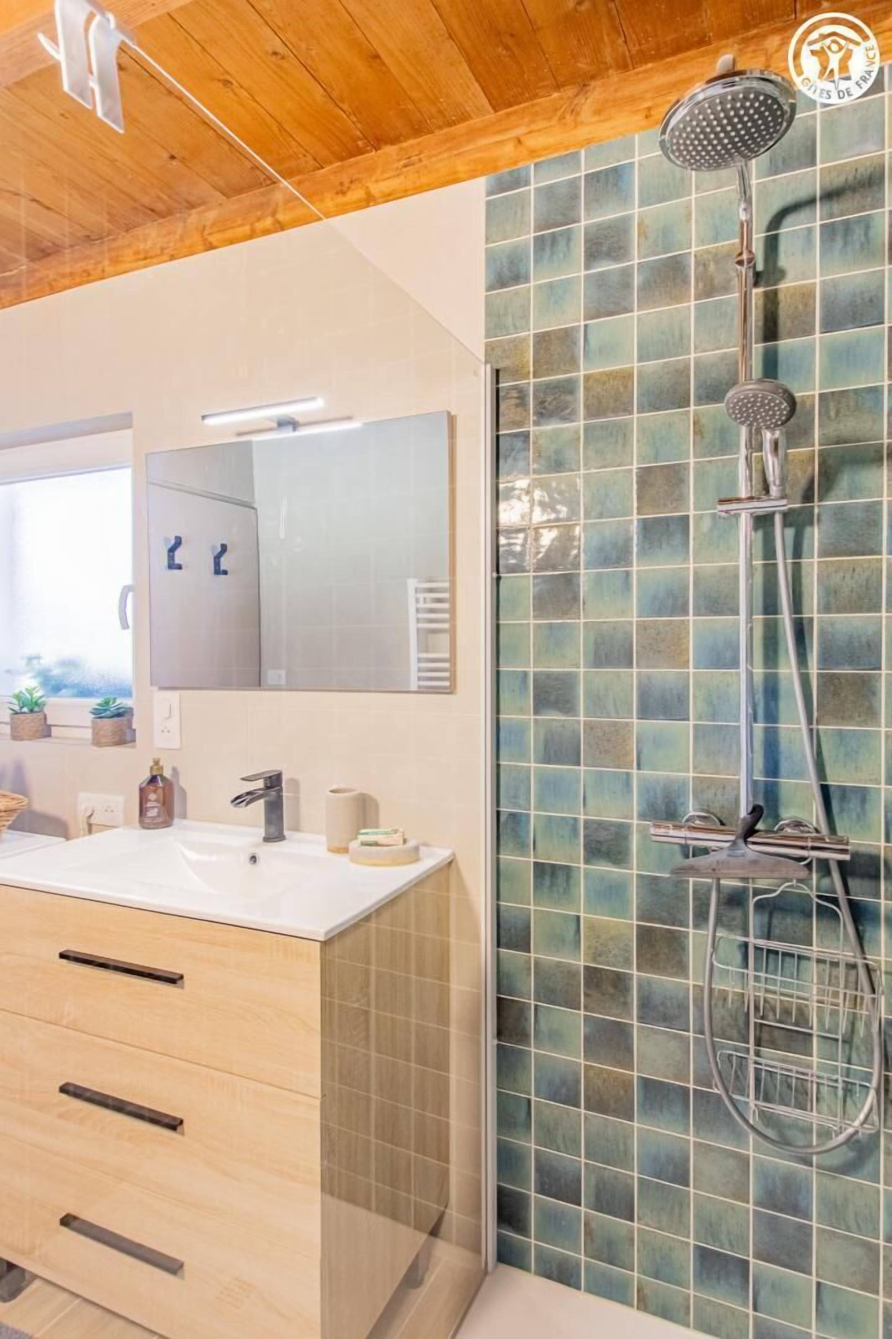 Un baño con techo de madera, un lavamanos blanco, un espejo y una ducha con pared de azulejos.