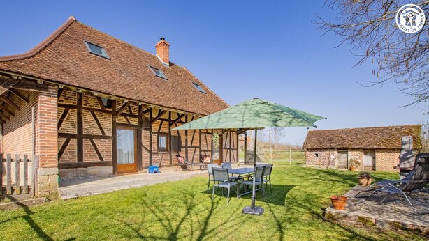 Une maison traditionnelle à colombages dotée d’un patio comprenant une table et des chaises, un parasol vert et un petit jardin.