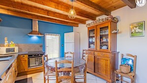 Une cuisine avec des meubles de rangement en bois, une table à manger avec des chaises, un réfrigérateur et un luminaire suspendu.
