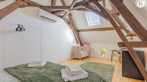 Une chambre mansardée chaleureuse, avec un plafond en pente, un berceau, un bureau et une fenêtre.