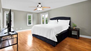 Ein Schlafzimmer mit einem Bett, einem Deckenventilator, einem Fernseher auf einem Schreibtisch und einer kleinen Pflanze.