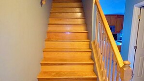 Eine hölzerne Treppe mit Geländer, die zu einer Zwischenebene mit blauer Wand und Fenster führt.