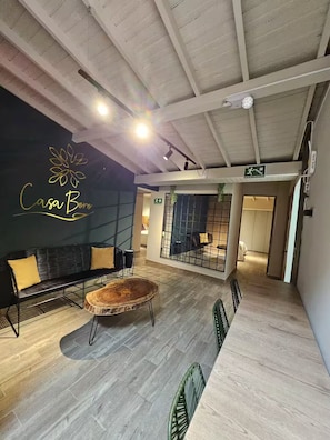 An interior with a sofa, chairs, a round wooden table, and a wall with a logo. - Boro House 6BR w/4Jacuzzis in Laureles (Medellín)