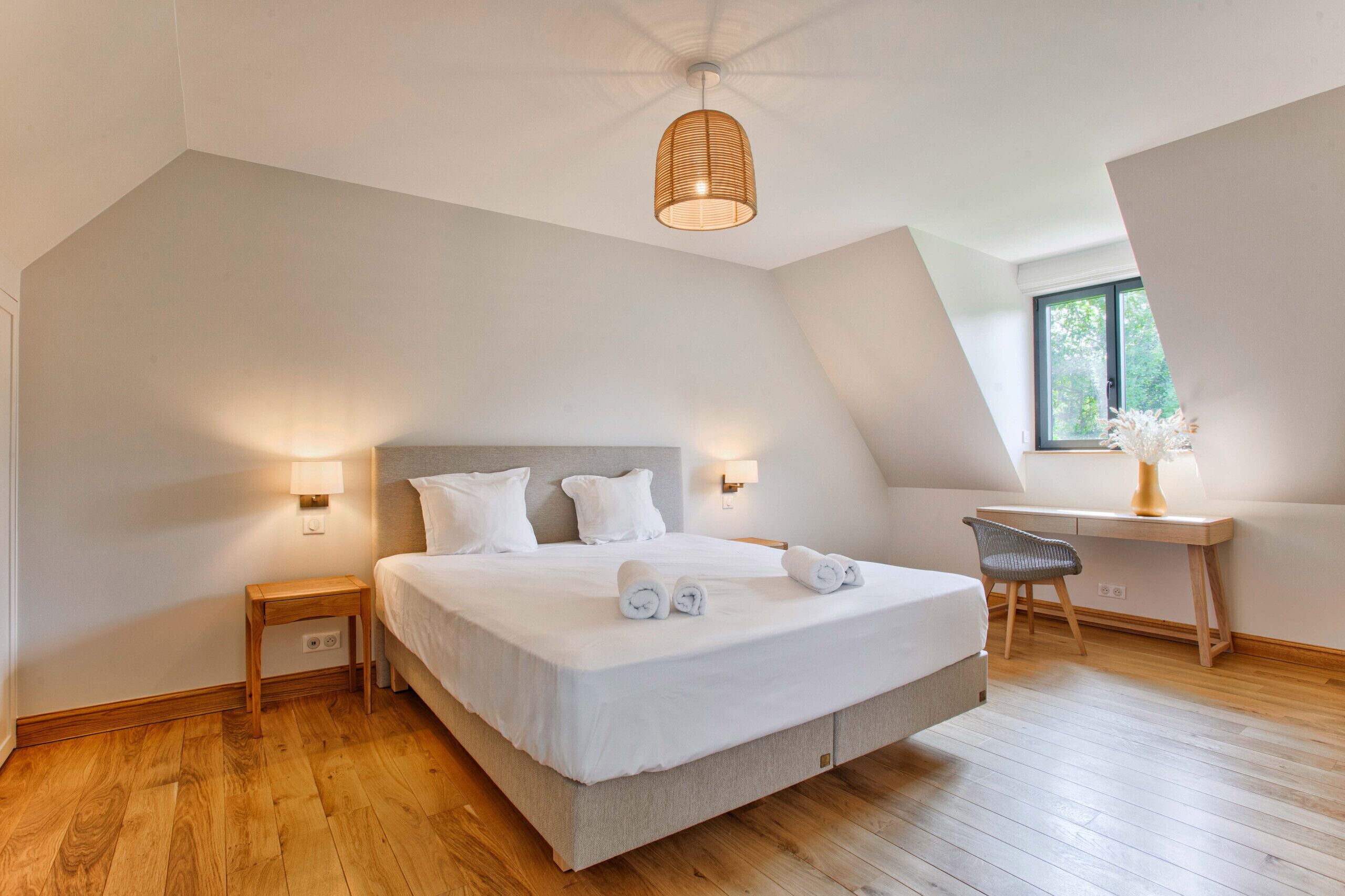 A bedroom with a large bed, bedside lamps, a desk, and a window.
