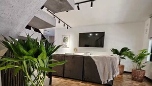 Un soggiorno moderno con pavimento in pietra, un divano ampio, una televisione a schermo piatto e piante in vaso.
