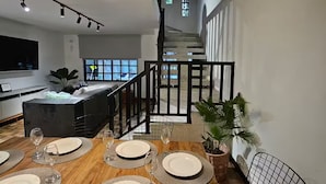 Zona pranzo con tavolo di legno apparecchiato per quattro persone, una scala e una cucina sullo sfondo.