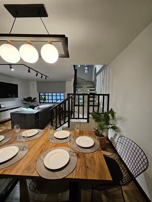 A dining area with a wooden table set for four, a staircase, and a kitchen in the background. - Magic Naranjo House 3BR w/AC & jacuzzi in Laureles (Medellín)