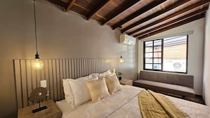 Una camera da letto con soffitto in legno, un letto grande con biancheria da letto bianca, una panca vicino alla finestra e due lampade a sospensione.