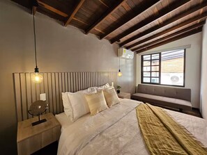 A bedroom with a wooden ceiling, a large bed with white bedding, a bench by the window, and two pendant lights. - Magic Naranjo House 3BR w/AC & jacuzzi in Laureles (Medellín)